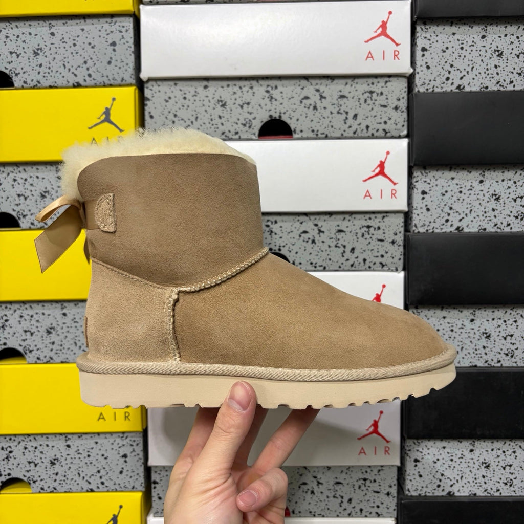 UGG Mini Bailey Bow Ankle Boot – Suede Boot with Cream Shearling Lining, Satin Bow Detail & Sand Sugar Sole in Sand